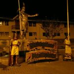Aguas Calientes: main square at night with a golden statue of an Inca ruler on a stone base, two smaller costumed figures and a Bienvenidos a Machupicchu sign