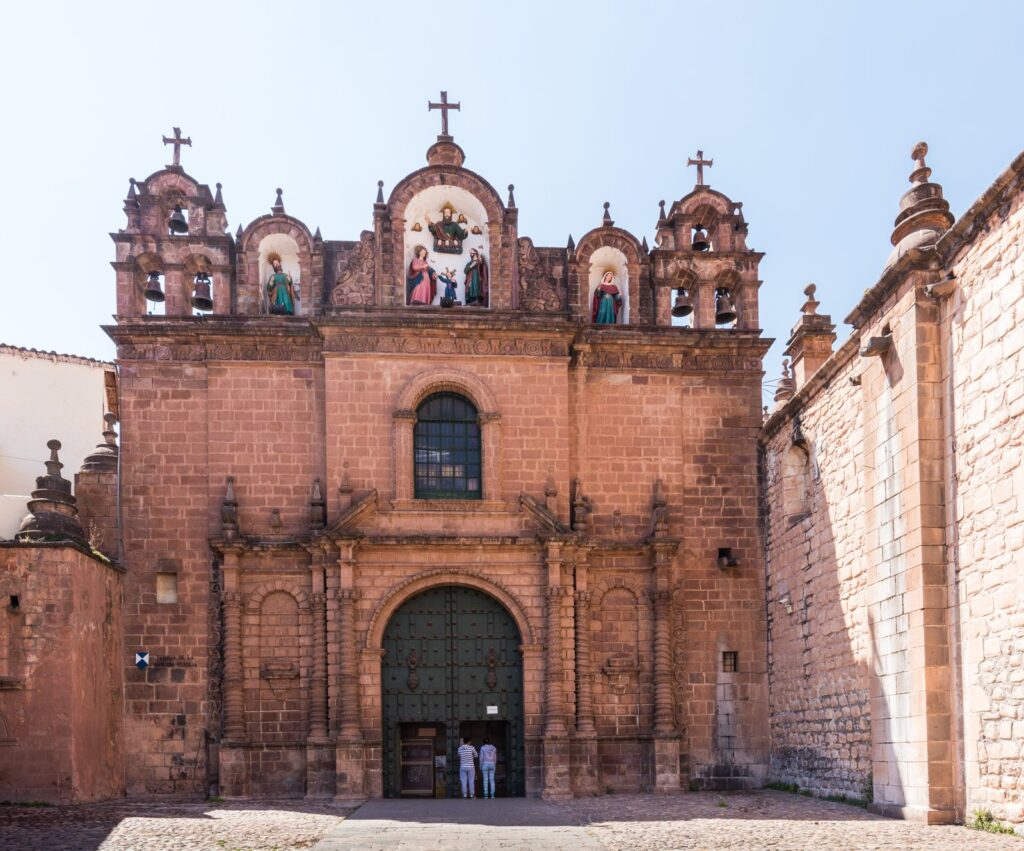 Stone church facade with arched green doors and bell gables on the Plaza de Armas in Cusco, under a clear blue sky
