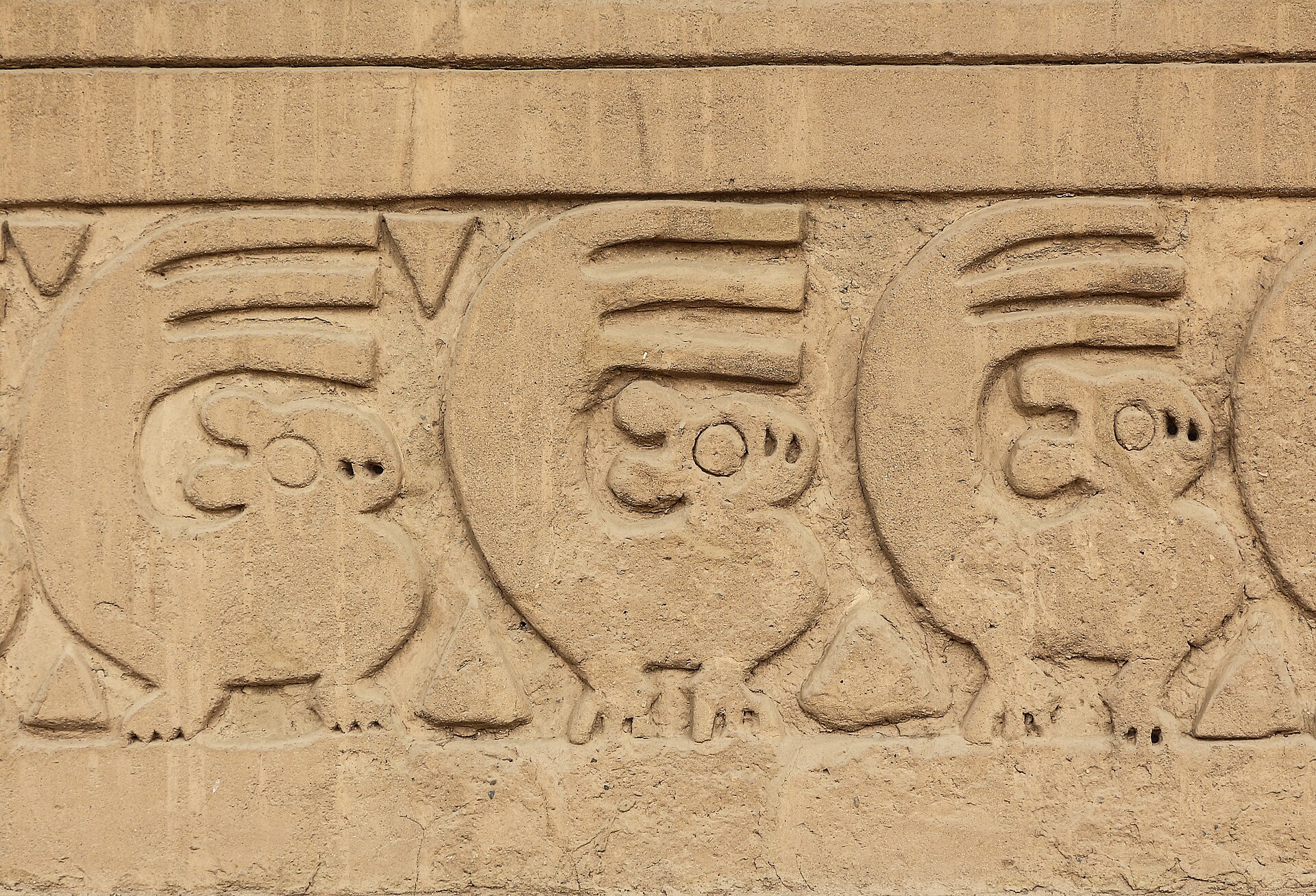 Chan Chan: carved earthen frieze with a row of repeated small animal figures and triangles on a sandy-colored adobe wall
