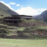 Chavin de Huantar: stone terraces and walls of the ancient temple on green grass, with steep mountains and a blue sky behind