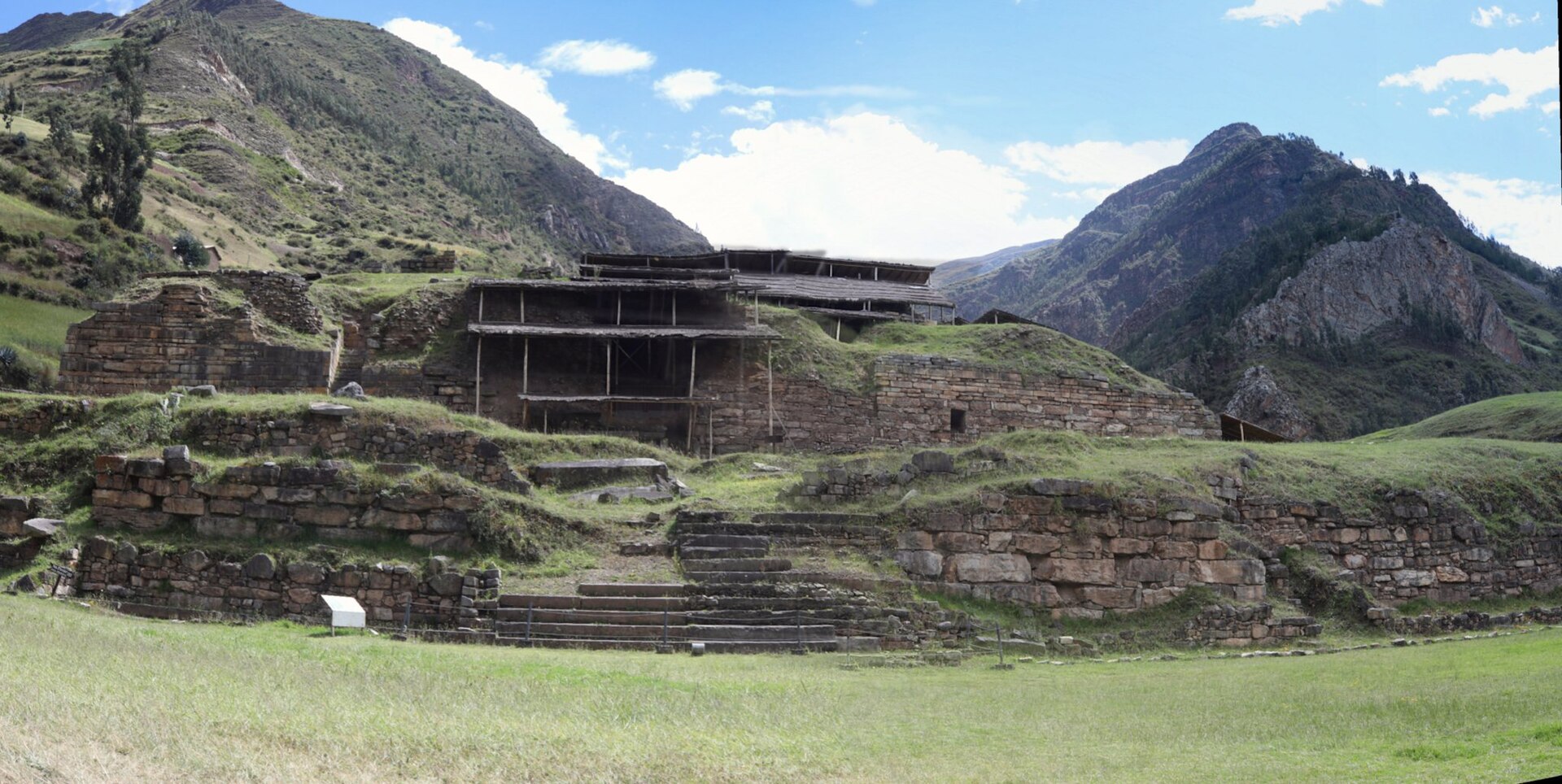 Chavin de Huantar: stone terraces and walls of the ancient temple on green grass, with steep mountains and a blue sky behind