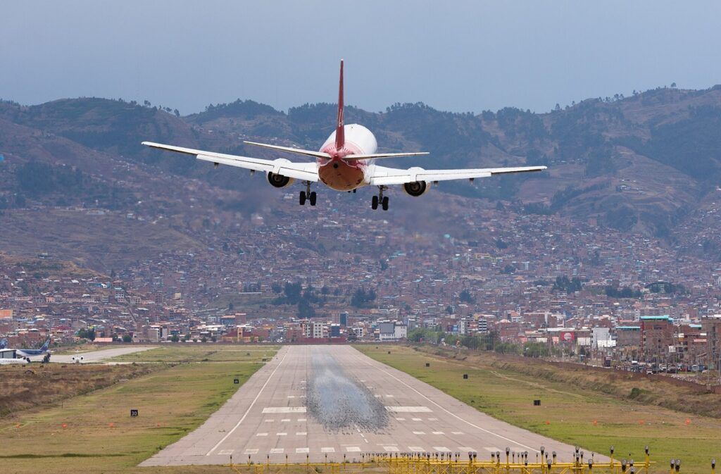 Passenger jet landing at Cusco airport with the city and Andean hills behind the runway