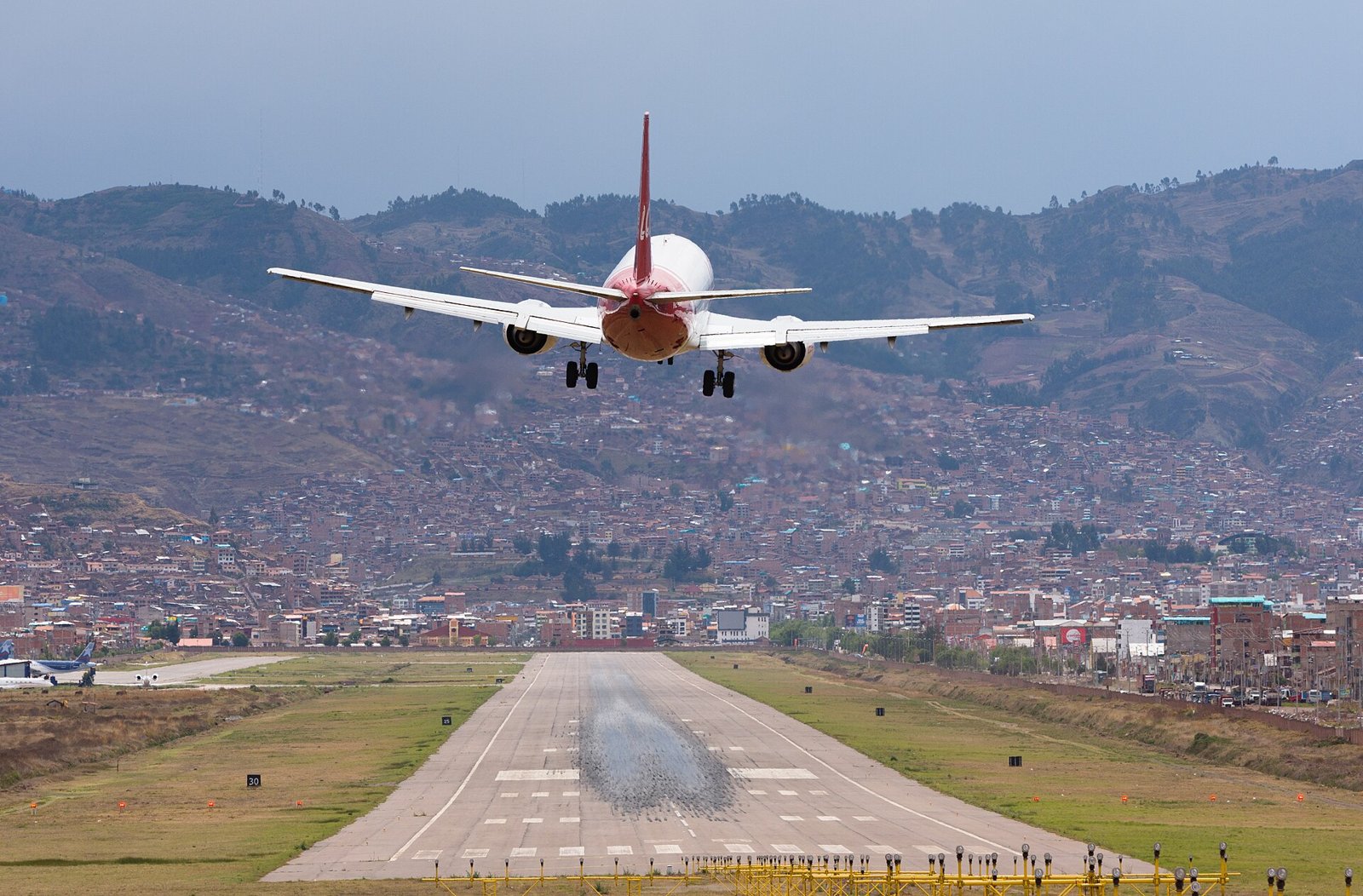 Passenger jet landing at Cusco airport with the city and Andean hills behind the runway