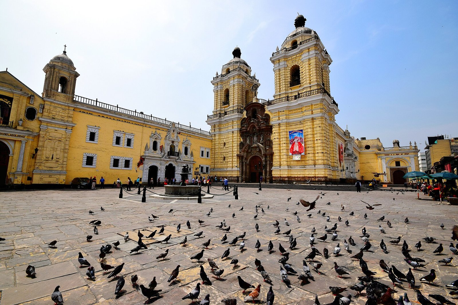 Yellow baroque Basilica and Convent of San Francisco in the Historic Centre of Lima, with pigeons in the plaza