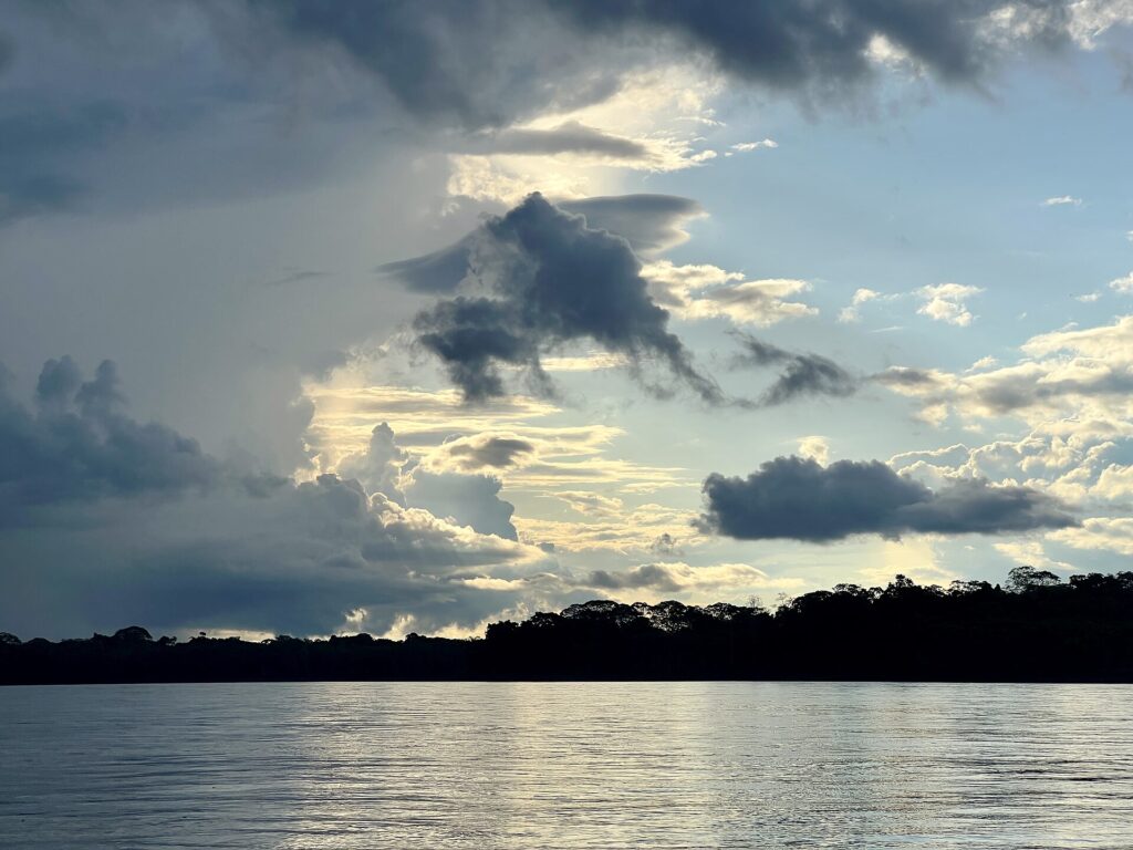 Wide river in the Peruvian Amazon at dusk, with a dark line of forest on the far bank under a cloudy sky