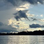 Wide river in the Peruvian Amazon at dusk, with a dark line of forest on the far bank under a cloudy sky