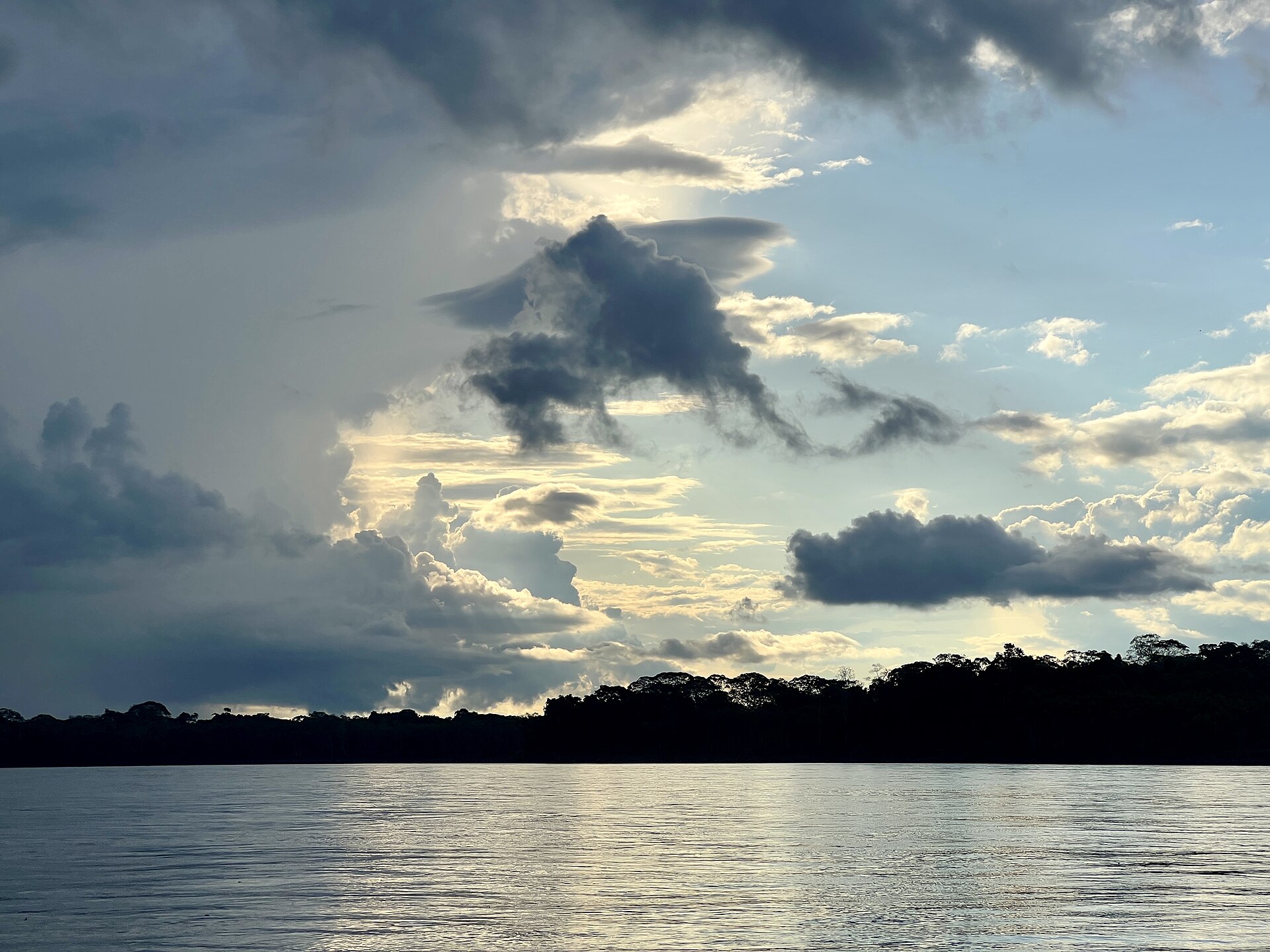 Wide river in the Peruvian Amazon at dusk, with a dark line of forest on the far bank under a cloudy sky