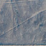 Nazca Lines from the air: the heron geoglyph with its long zigzag neck and a long straight line crossing the pale desert ground