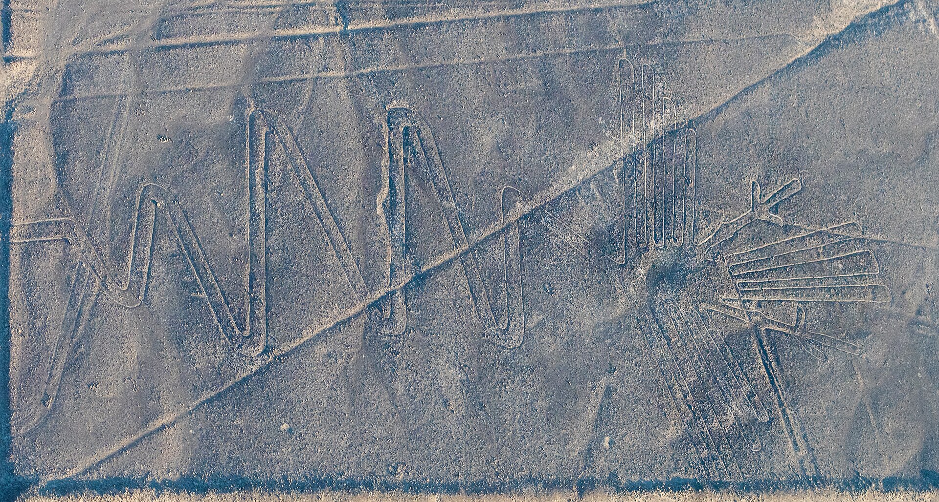 Nazca Lines from the air: the heron geoglyph with its long zigzag neck and a long straight line crossing the pale desert ground