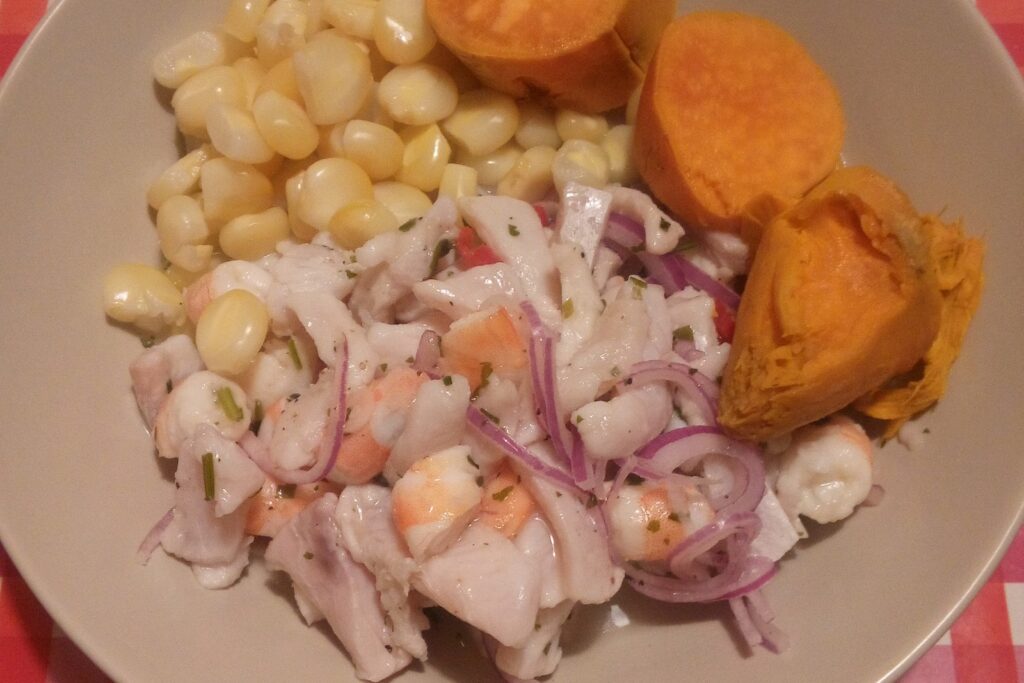 Plate of Peruvian ceviche with fish, red onion, chili and sides on a dark table