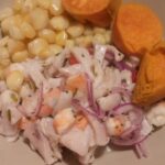 Plate of Peruvian ceviche with fish, red onion, chili and sides on a dark table