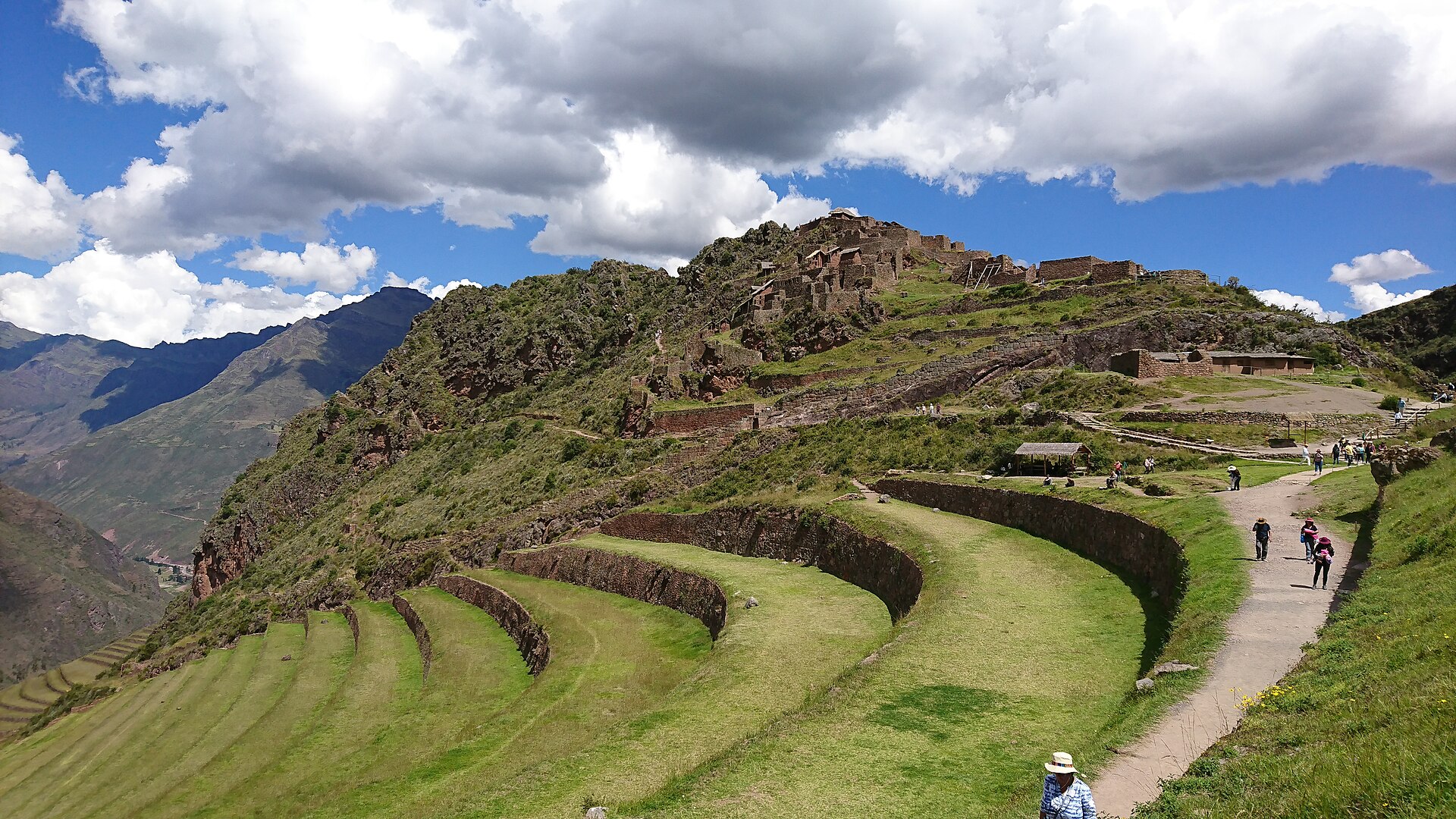 Sacred Valley day trip stop at Pisac: green Inca terraces curving around a hillside, with a footpath, hikers and mountains