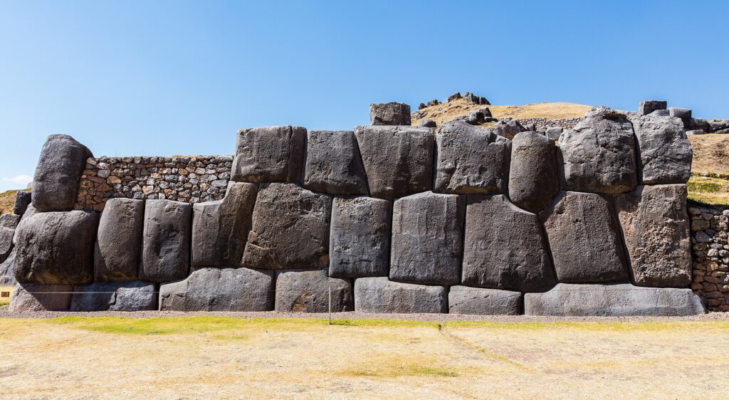 Huge fitted Inca stone wall at Saqsayhuaman, a site on the Cusco Tourist Ticket, with dry grass in front and a clear blue sky