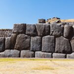 Huge fitted Inca stone wall at Saqsayhuaman, a site on the Cusco Tourist Ticket, with dry grass in front and a clear blue sky